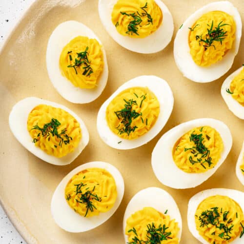 Deviled eggs with dill sprinkled on top, on a yellow decorative plate.