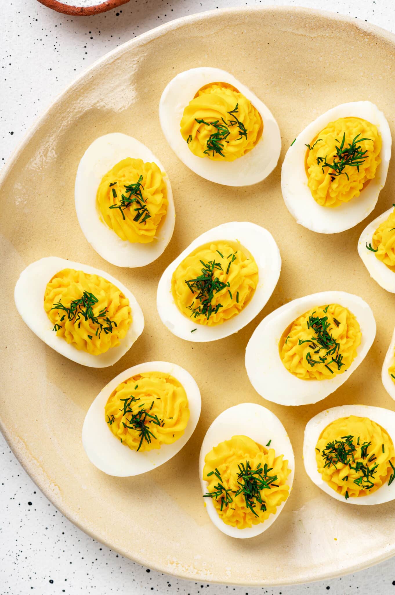 Deviled eggs with dill sprinkled on top, on a yellow decorative plate.