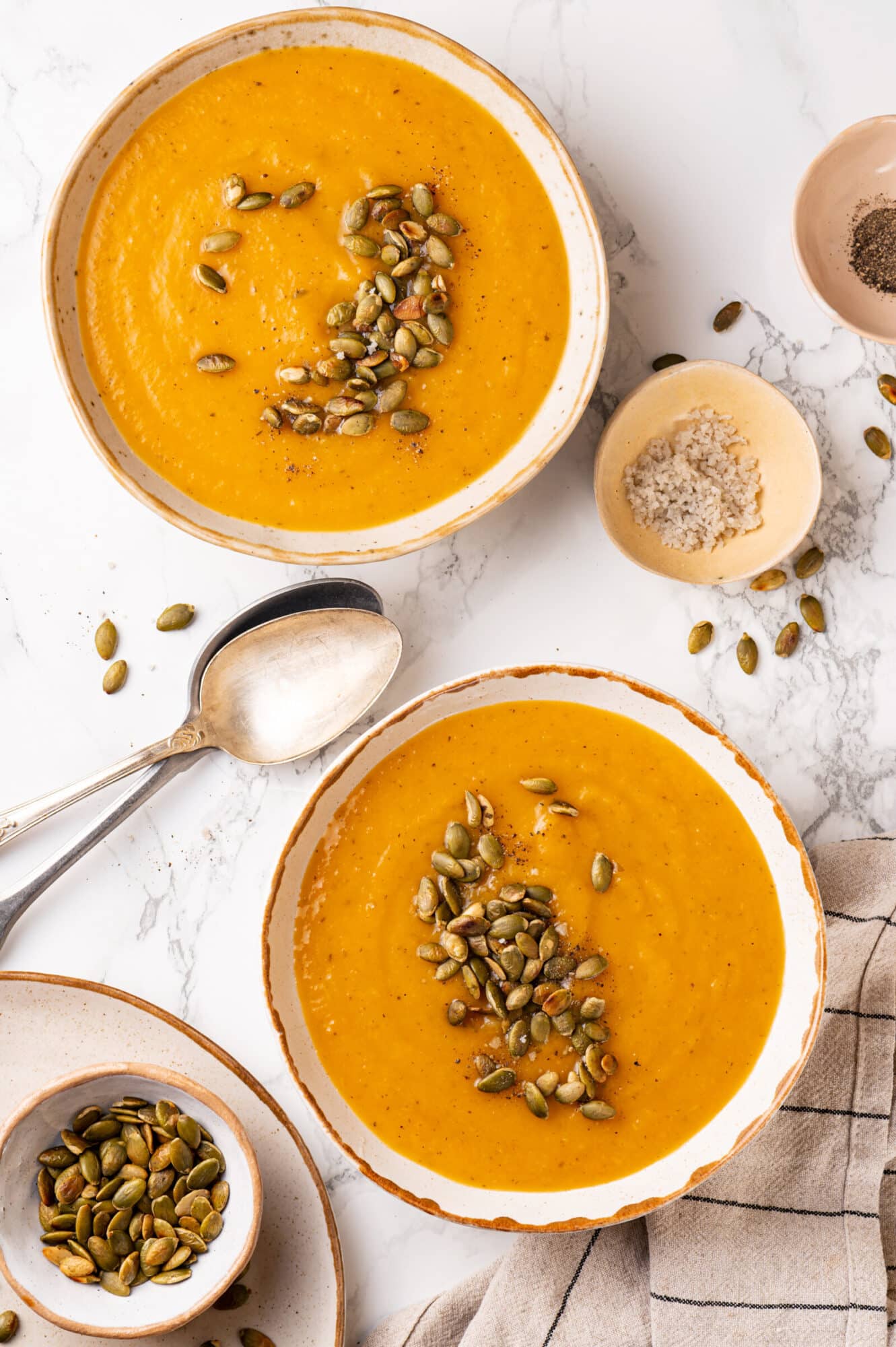 Pumpkin seeds atop bowls of winter squash soup with a spoon for serving.