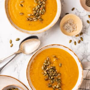 Pumpkin seeds atop bowls of winter squash soup with a spoon for serving.