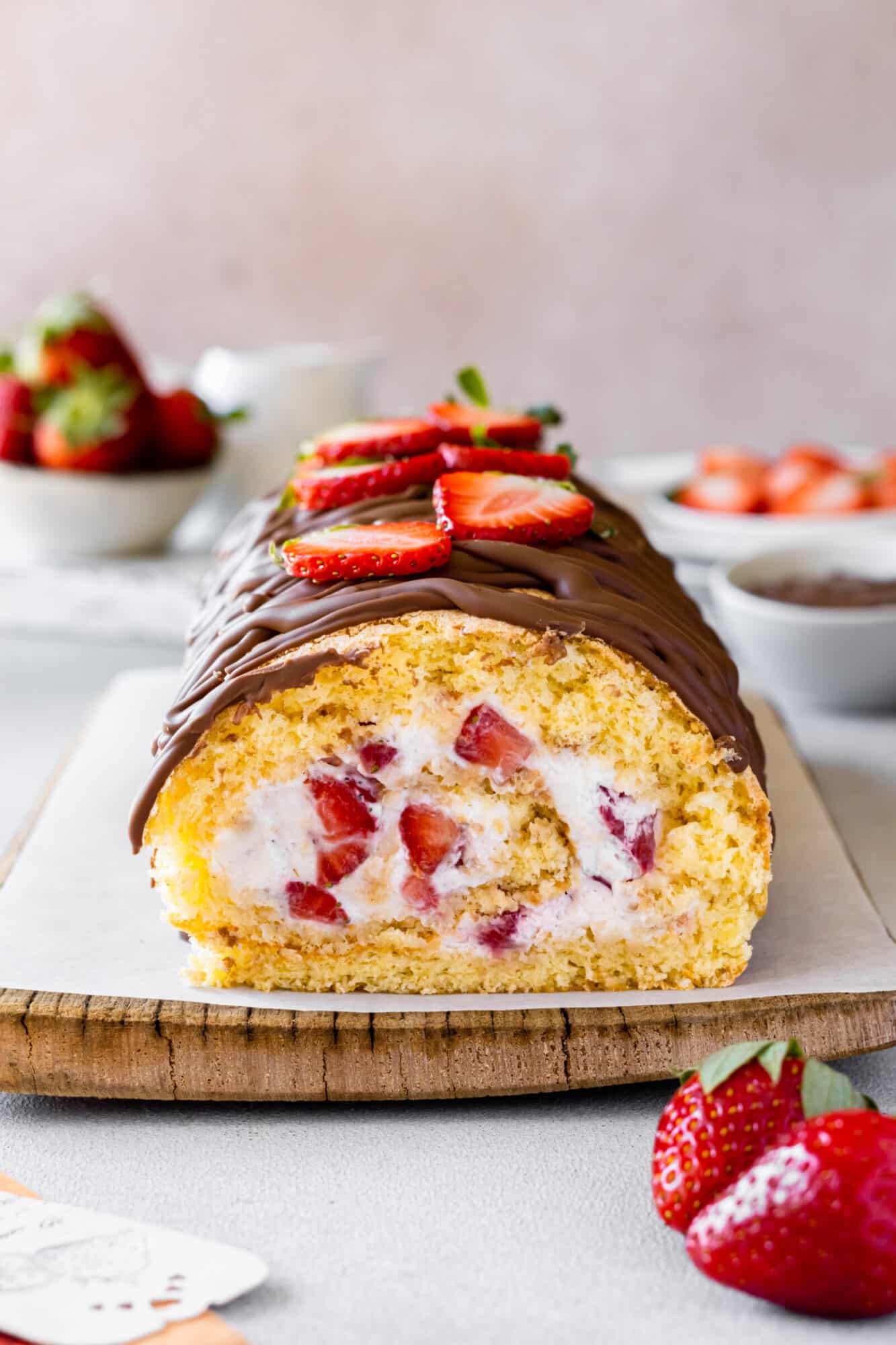 Strawberry cake roll on a wooden board with more strawberries on the side.