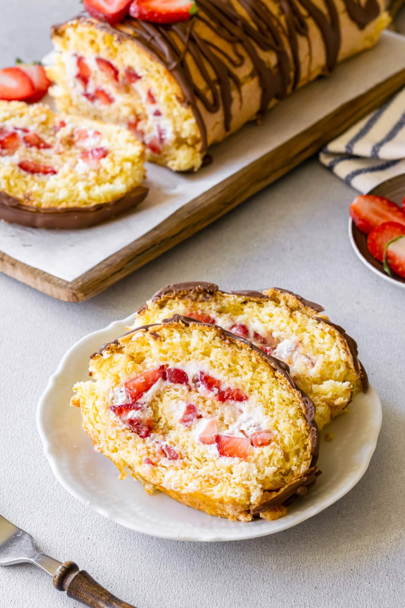 Strawberry cake roll slices on a plate with more cake roll in the background.