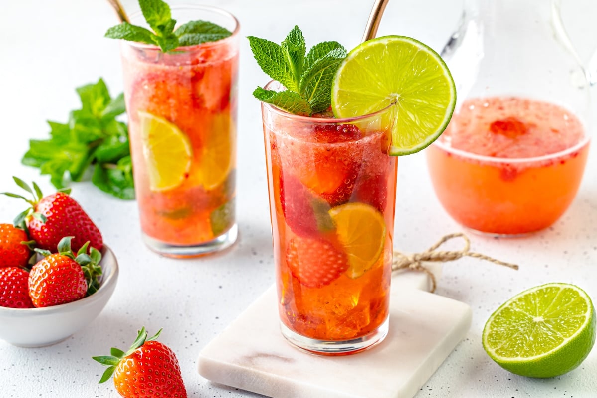 strawberry mojito mocktail drink in two glass cups with slice fresh lime on a white board.