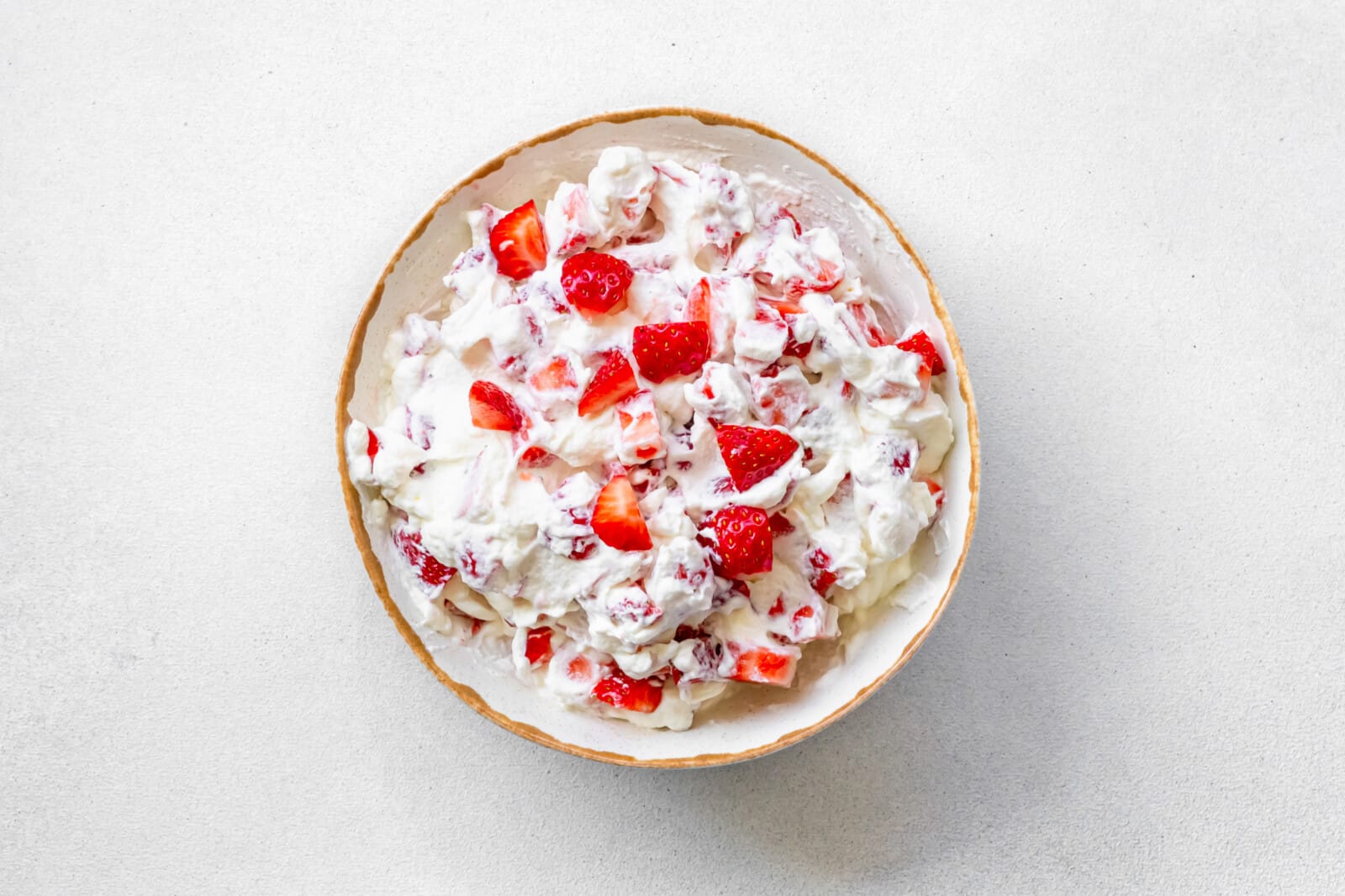 Strawberry pieces in frosting cream in a bowl.