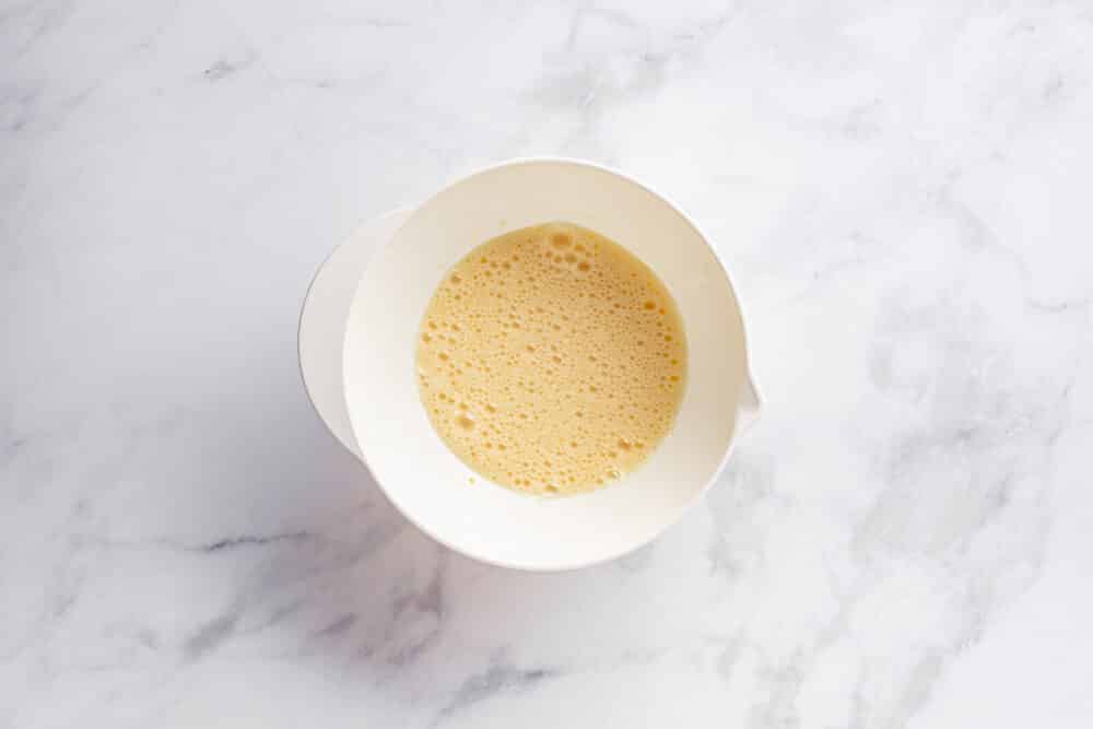 Eggs and sugar mixed in a white bowl.