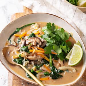 Thai coconut soup in a bowl on a wooden board with a gold spoon on the side.