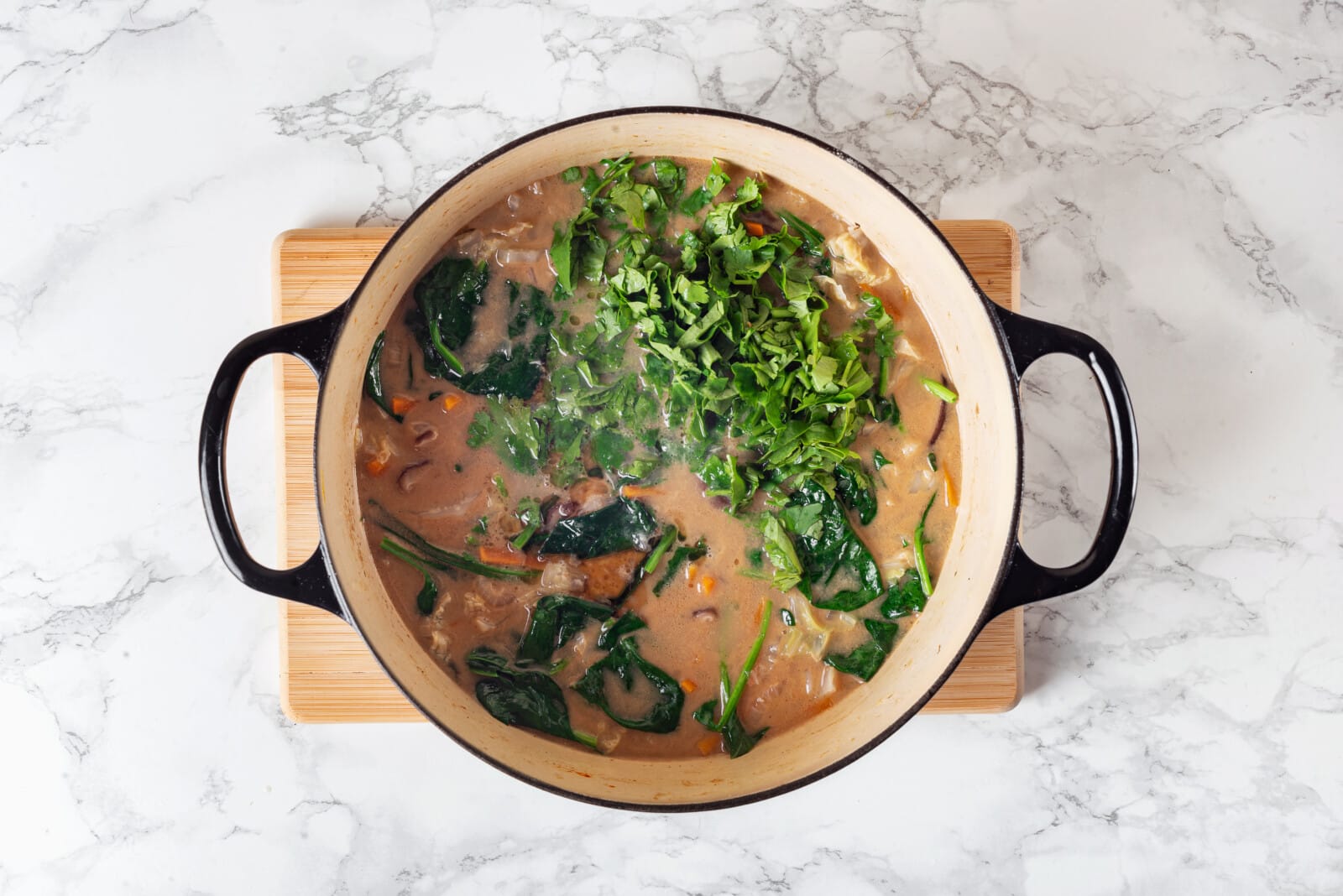 Cilantro and lime added to Thai coconut soup pot on a wooden board.