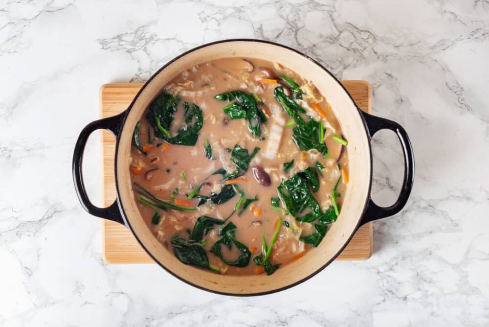 Thai coconut soup cooking in a black pot on a wooden board.