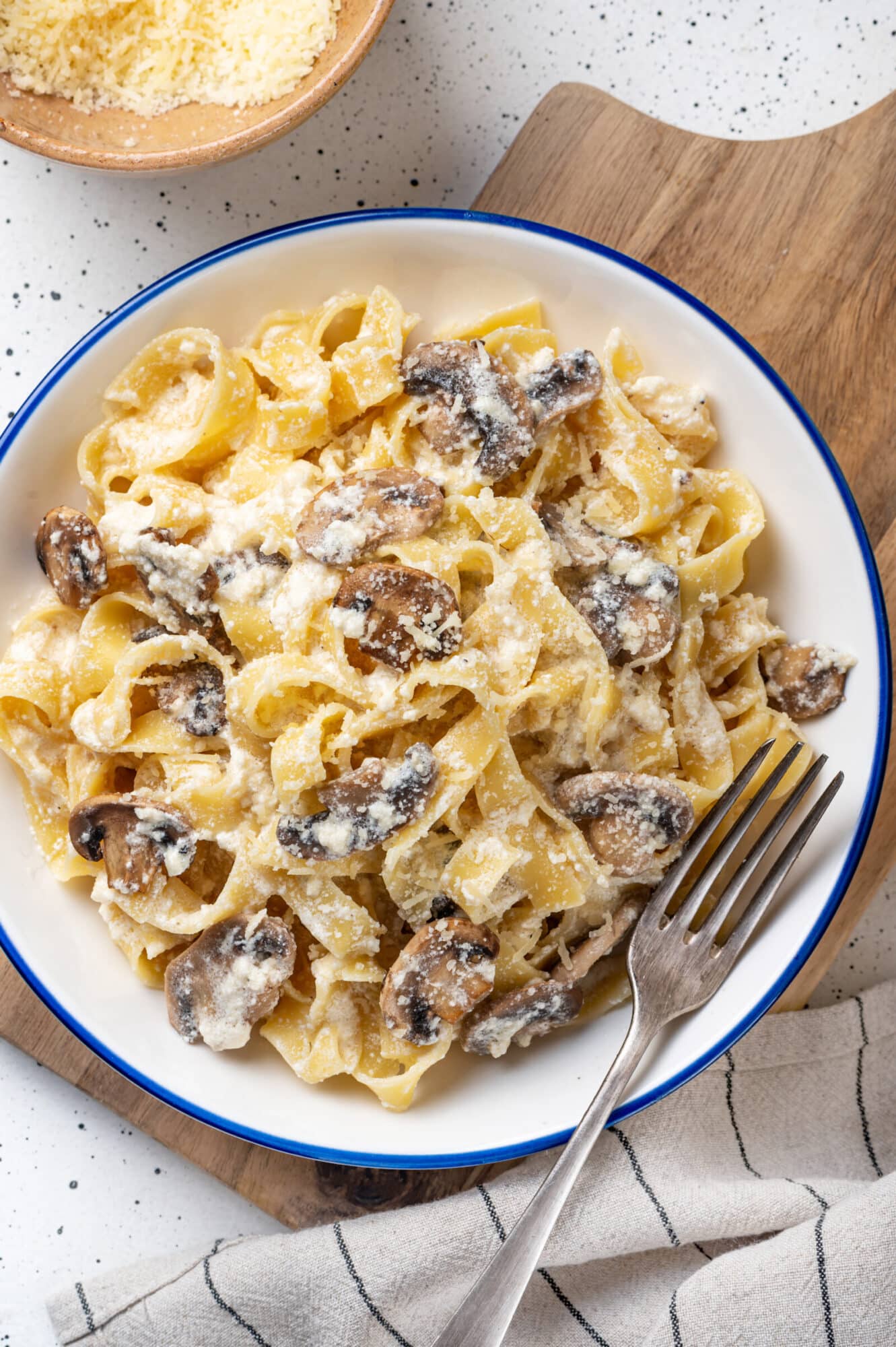 Top view of mushroom alfredo pasta serving on a white plate with a blue rim.