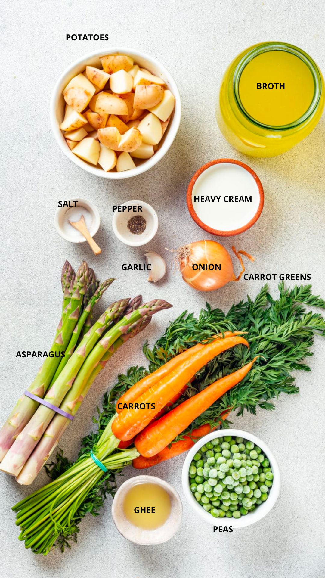 vegetarian asparagus soup ingredients spread with labels- potatoes, broth, salt, pepper, garlic, onion, heavy cream, carrots, carrot greens, asparagus, ghee, and peas.