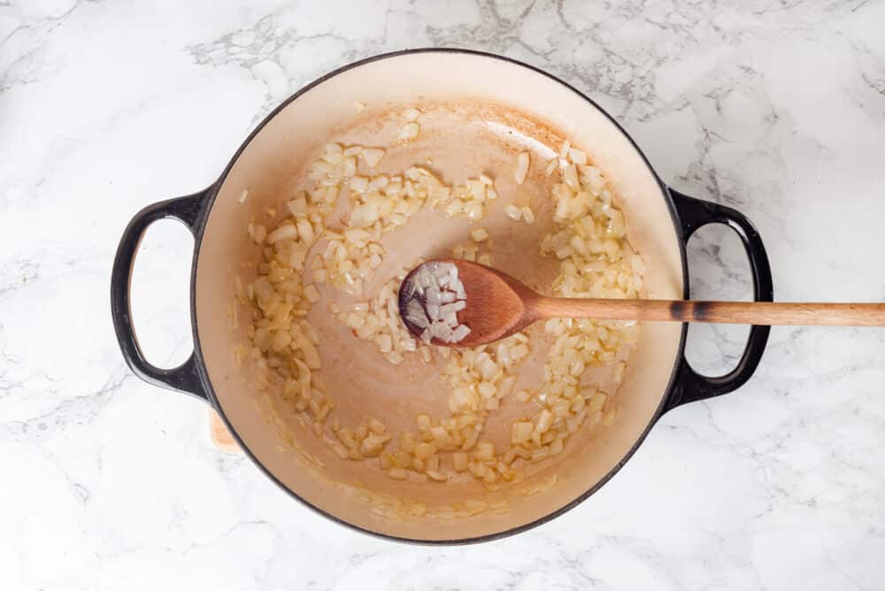 Onion sautéing in a soup pot with a wooden spoon.