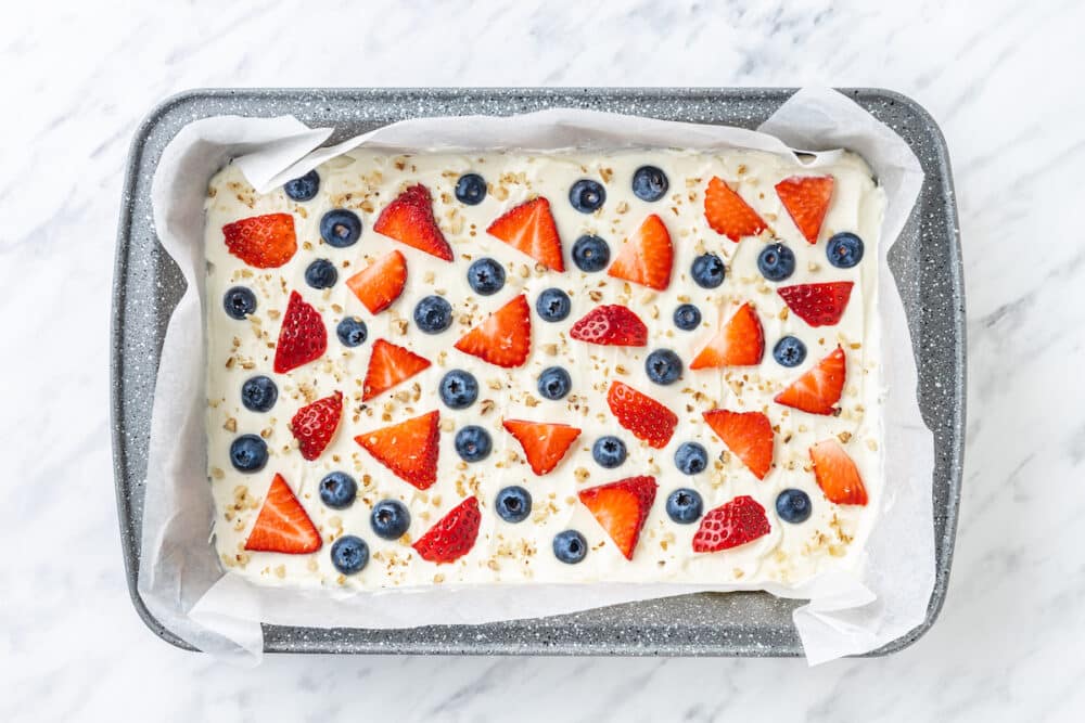 yogurt bark with sliced strawberries and whole blueberries in a pan with chopped sprinkled walnuts.