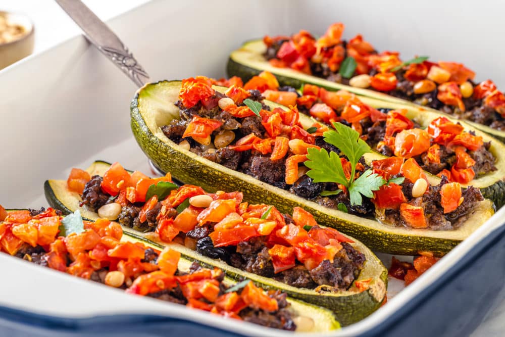 boats of stuffed zucchini laying baked in a baking dish.