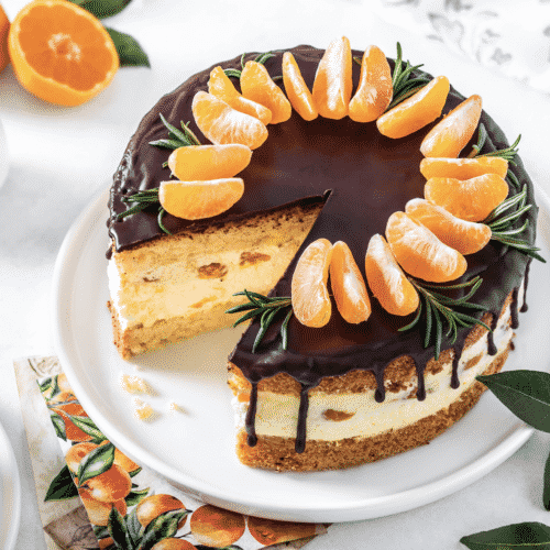 Mandarin mousse cake on a white plate with mandarins decorating the top.